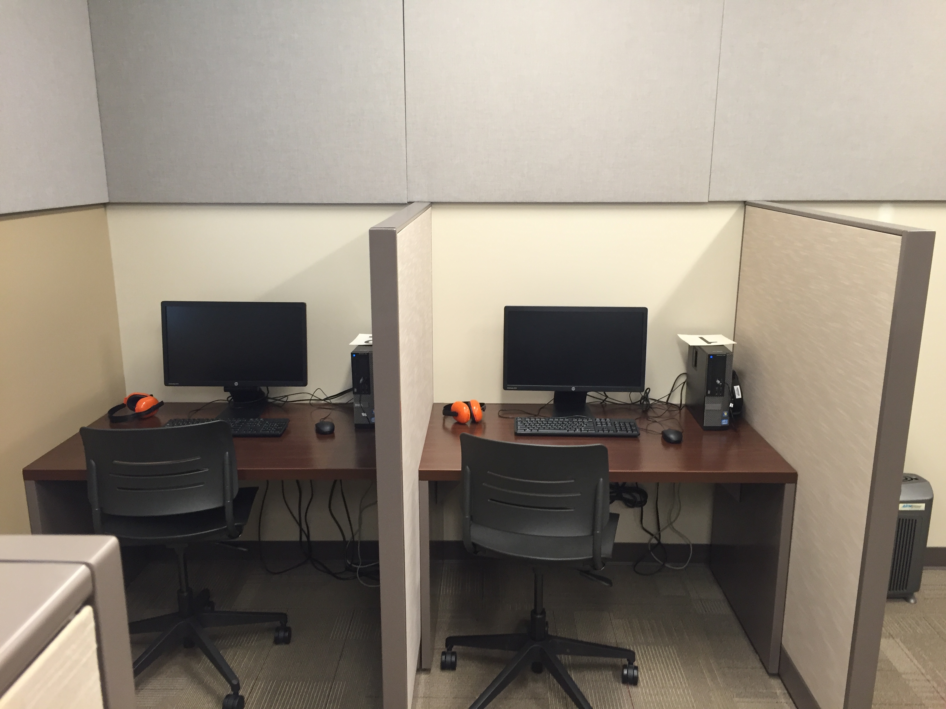Two cubicles with computers, desks, and office chairs with orange headphones sitting to left of the computer.