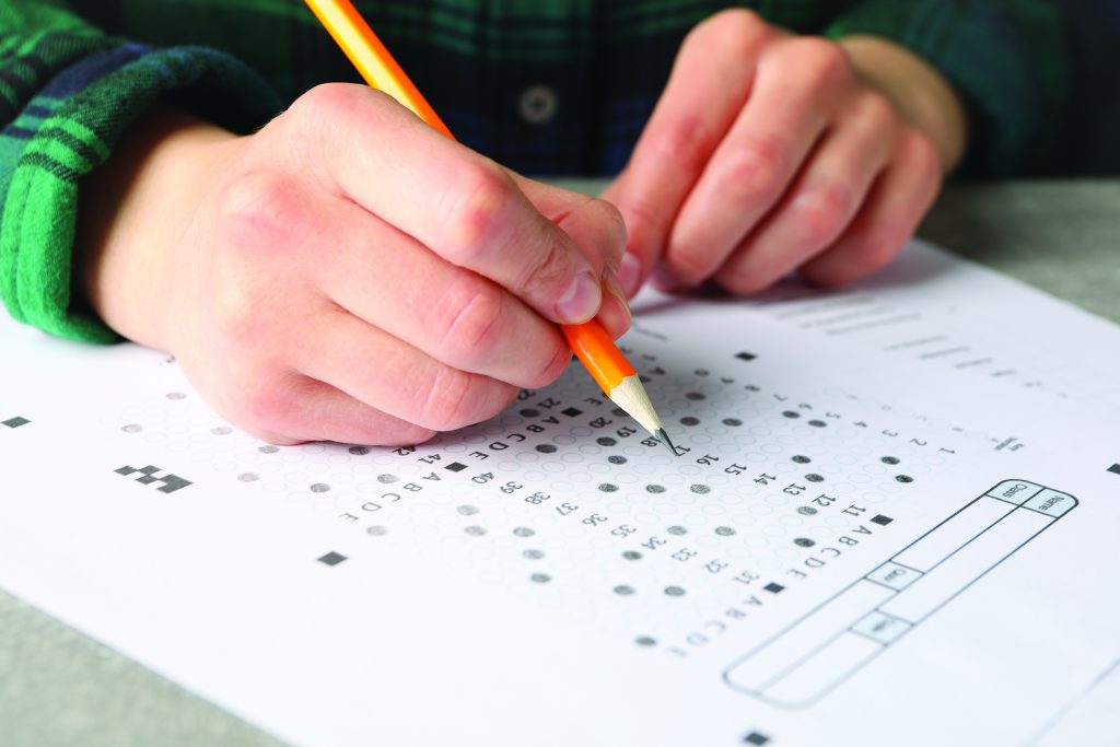 A close up of a woman filling out a test scantron sheet on grey table